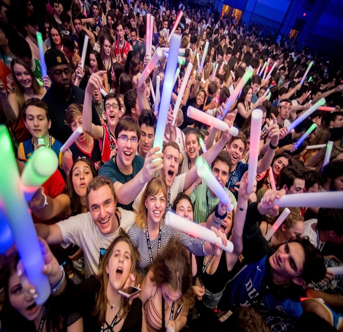 A diverse crowd of people celebrating at a concert, raising their hands and cheering.